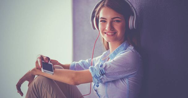 Smiling girl with headphones sitting on the floor near wall - Foto, Bild