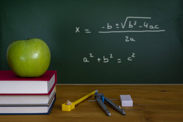 Concept de classe de mathématiques avec pomme verte sur pile de livres et compas de dessin avec équation sur tableau noir
 - Photo, image
