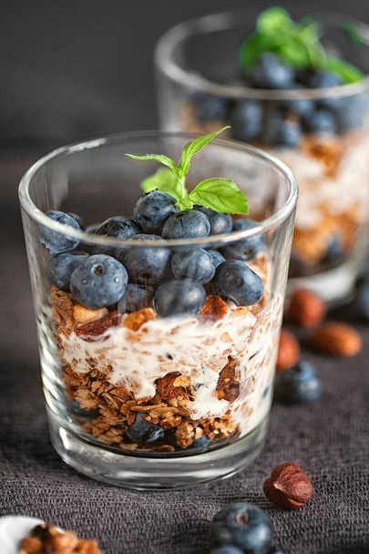 Σπιτικά μούσλι πρωινό με blueberries και γιαούρτι, που σερβίρεται στα γυαλιά πάνω από ένα γκρίζο φόντο - Φωτογραφία, εικόνα