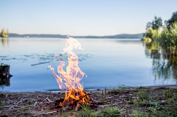 Beautiful campfire in the evening at lake. Fire burning in dusk at campsite - Foto, afbeelding