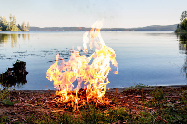 Beautiful campfire in the evening at lake. Fire burning in dusk at campsite - Fotoğraf, Görsel