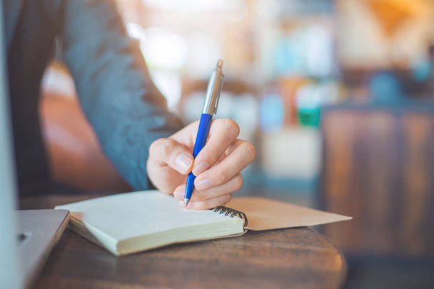 Femme d'affaires écriture à la main sur un bloc-notes avec un stylo dans le bureau
. - Photo, image