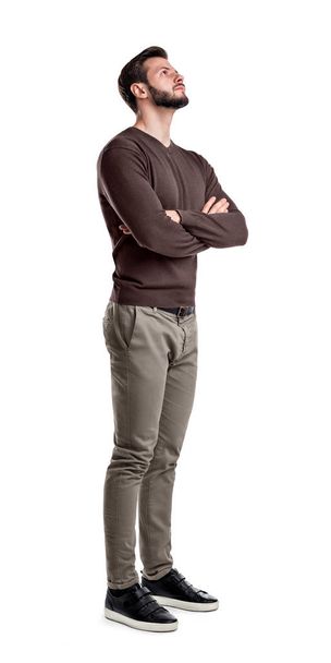Een bebaarde man in smart casual kleding staat in half-bocht met armen gevouwen en kijkt naar boven. - Foto, afbeelding