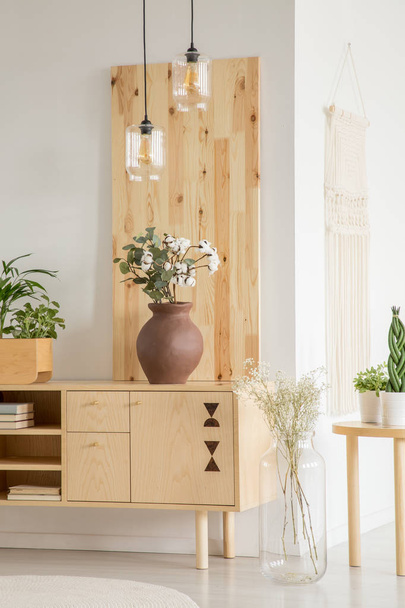 Lamps above wooden cupboard with flowers in white simple living room interior. Real photo - Фото, зображення