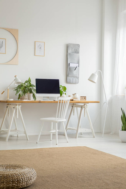 White chair at desk with desktop computer in home office interior with pouf on carpet. Real photo - 写真・画像