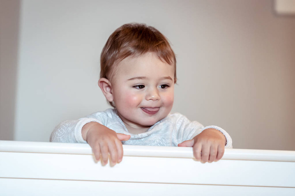 Sweet baby boy standing in his nice white cot, little child in sleepwear in the kidsroom at home, preparing to nap, happy carefree childhood - Photo, Image