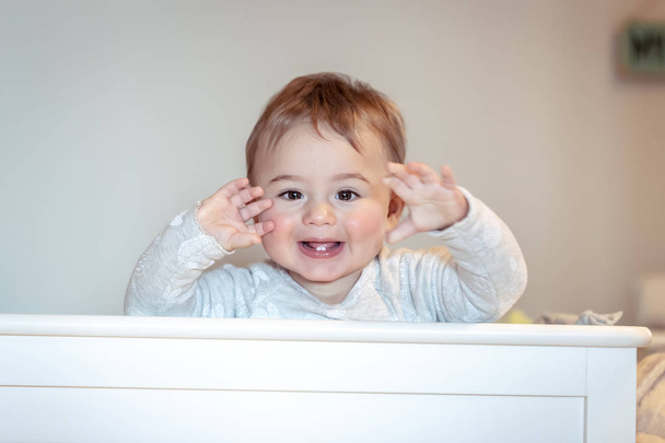 Portrait of a cute little baby boy at home in the crib making faces, sweet child having fun in his bedroom, happy healthy childhood  - Photo, Image