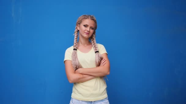 ernsthafte blonde Hipster-Studentin blickt mit verschränkten Armen vor blauem Hintergrund in die Kamera - Filmmaterial, Video