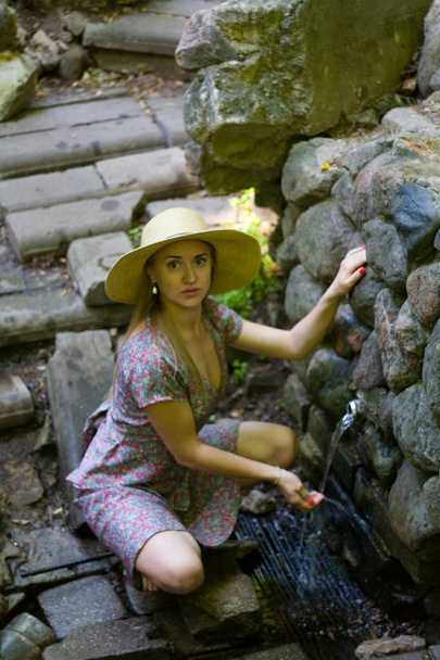 Beautiful girl in a hat next to a natural source. Human and nature. - Fotoğraf, Görsel