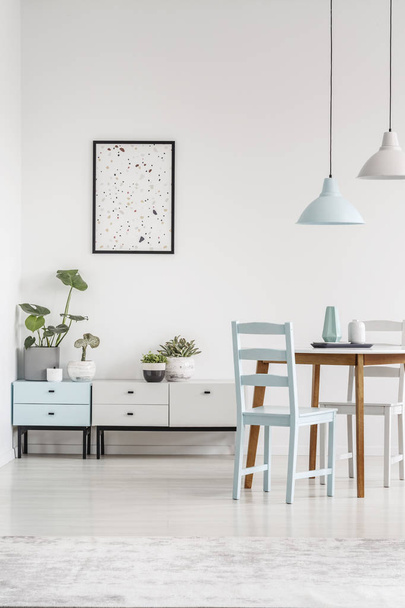Real photo of low cabinets, graphic on the wall and dining table with chairs in a bright dining room interior - Valokuva, kuva