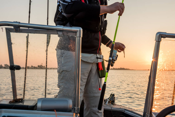 Ο ψαράς με ένα περιστρεφόμενο στα χέρια του από το καράβι αλίευση την αυγή. - Φωτογραφία, εικόνα