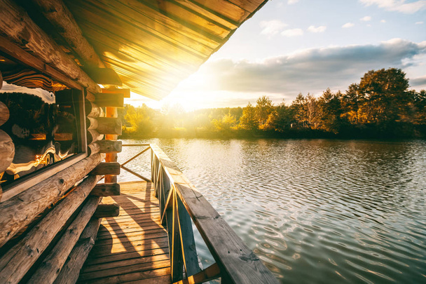 Wooden house with a terrace on the water at the lake, at sunset, a beautiful river bank at sunset - Фото, зображення