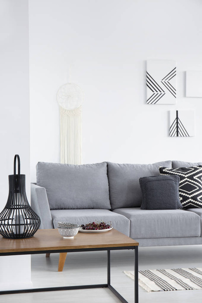 Pillows on grey couch and lanterns on table in minimal living room interior with posters. Real photo - Photo, image