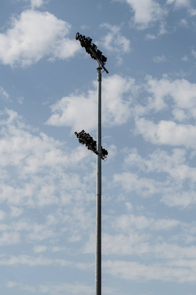 Um poste alto encimado por holofotes perto de um campo esportivo
 - Foto, Imagem