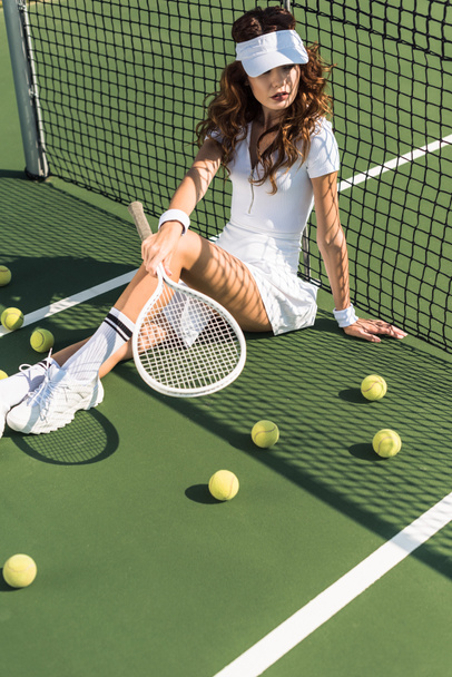 テニスコートでネットで座っているテニス ラケットで白スポーツウェアでスタイリッシュなテニス選手 - 写真・画像