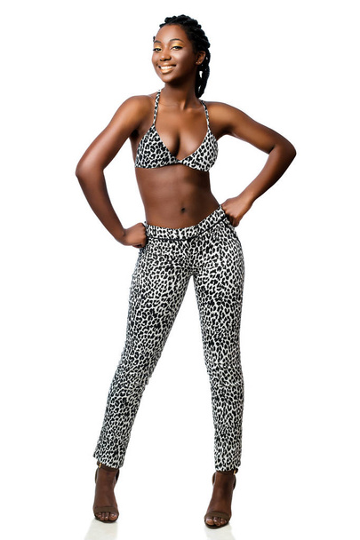 Full length portrait of attractive african woman wearing leopard pants and bikini top standing with hands on hips isolated on white background  - Photo, Image