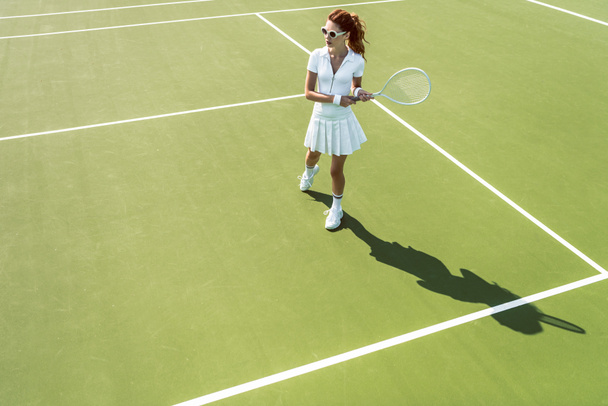 Zijaanzicht van jonge aantrekkelijke vrouw in witte tennis uniforme tennissen op Hof - Foto, afbeelding