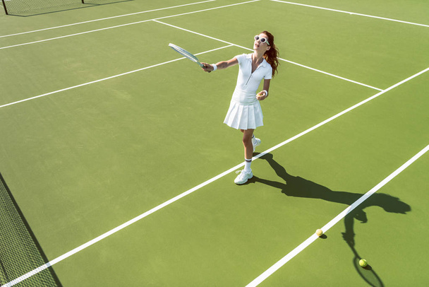 вид сбоку молодой привлекательной женщины в белой теннисной форме, играющей в теннис на корте
 - Фото, изображение