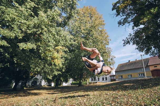 Boy practicing free runnuing in public park and jumping upside down. - Фото, изображение