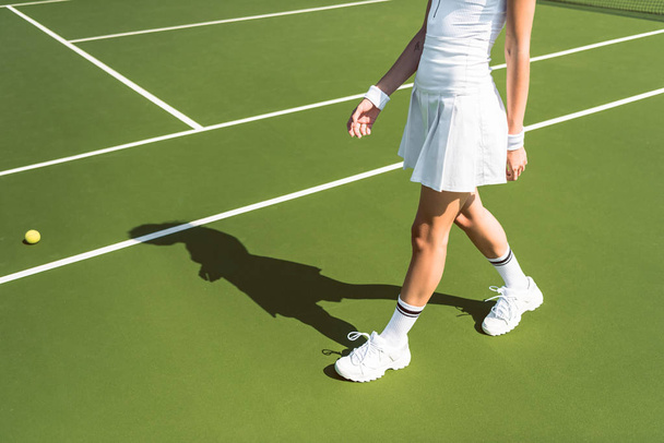 cropped shot of female tennis player in white sportswear walking on tennis court - Valokuva, kuva
