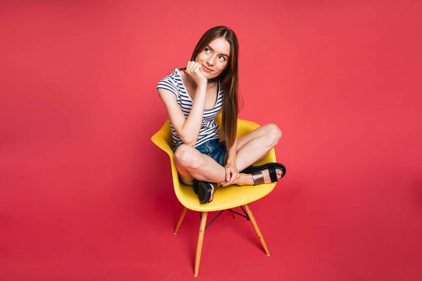 Portrait of young girl sitting on chair on red background - Foto, imagen