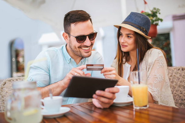Sorprendida pareja joven haciendo compras en línea a través de tableta digital con tarjeta de crédito en la cafetería
 - Foto, Imagen