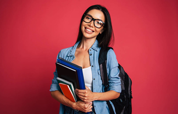 Portrait of young brunette posing with note books on red background  - Foto, afbeelding