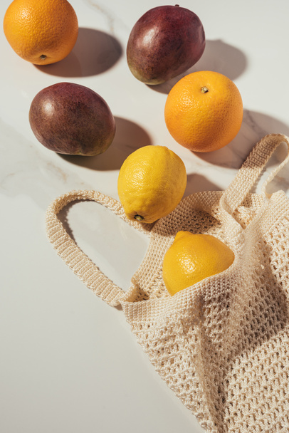 верхний вид на струнный мешок со свежими спелыми тропическими фруктами на белом
 - Фото, изображение
