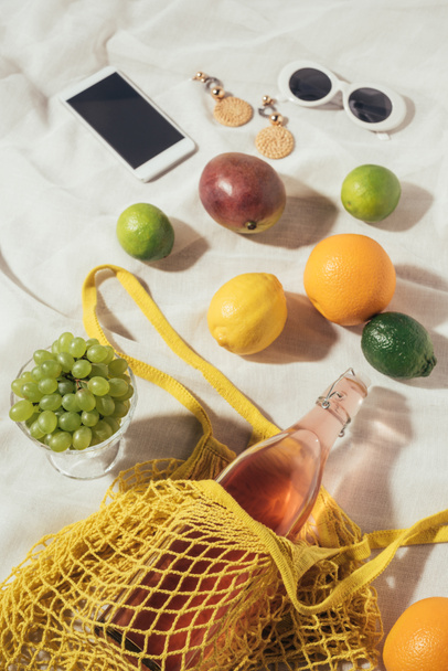 visão de alto ângulo do smartphone, óculos de sol, brincos e saco de cordas com frutas frescas
 - Foto, Imagem