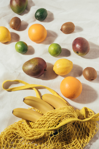 hoge hoekmening van gele tekenreeks tas en vers rijp tropisch fruit - Foto, afbeelding