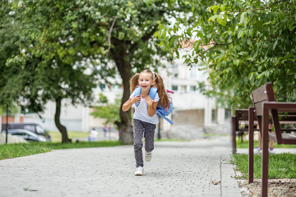 The little schoolgirl is running with a backpack and laughing. The concept of school, study, education, friendship, childhood. - Valokuva, kuva