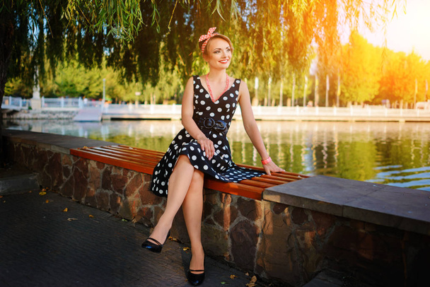 Uma bela jovem vestida senta-se em um banco perto da lagoa
. - Foto, Imagem