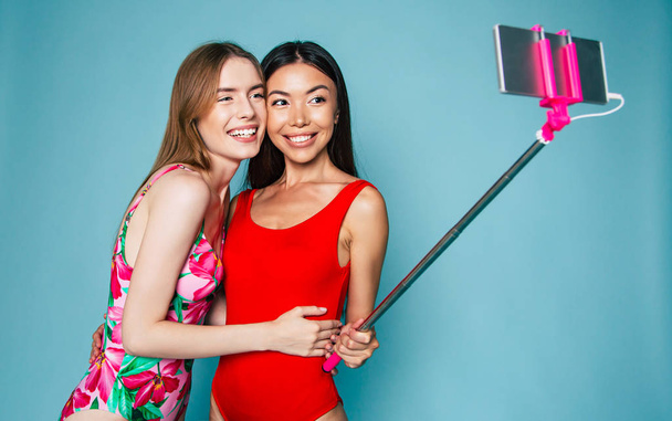Portraits of young girls making selfie on smartphone on blue background - Фото, изображение