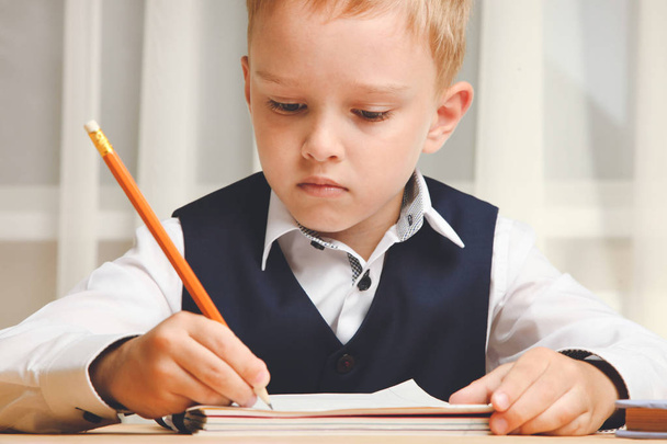 Uczniak siedzi przy biurku i pisze w notesie. Koncepcja szkoły. - Zdjęcie, obraz