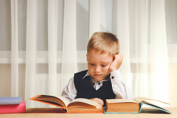 Schoolboy sits at table and reads lot of books. Concept school. - Foto, immagini