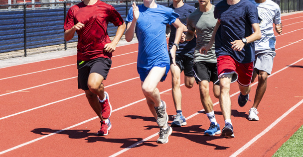 Un groupe de lycéens courent et s'entraînent ensemble sur une piste rouge sous le soleil éclatant de l'été
. - Photo, image