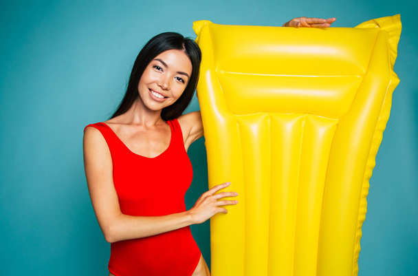Portrait of young brunette posing with yellow air mattress on blue background  - Foto, immagini