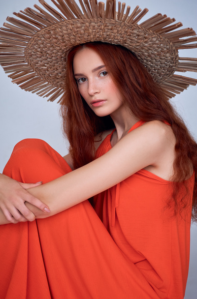 stylish woman with red hair posing in dress and straw hat, isolated on grey - Photo, Image
