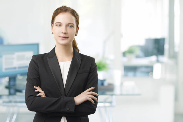 Shot of a smiling young businesswoman standing in the office with arms crossed.  - 写真・画像