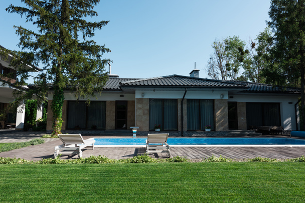 vista de la casa moderna, junto a la piscina con tumbonas y césped verde
 - Foto, Imagen