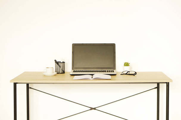Laptop ohne Bildschirm, Tasse Cappuccino, Kaktus, Zubehör und zusammengefaltete Brille auf einem Holztisch in einem geräumigen Büro voller Sonnenlicht. kreativer Arbeitsbereich. Nahaufnahme, Kopierraum, Hintergrund - Foto, Bild