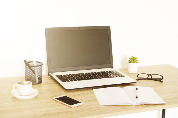 Ordenador portátil de pantalla en blanco, taza de café capuchino, cactus, suministros y gafas plegadas en escritorio de madera en una espaciosa oficina llena de luz solar. Espacio de trabajo creativo. Cerrar, copiar espacio, fondo
 - Foto, Imagen