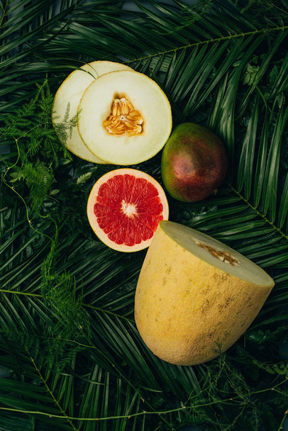 bovenaanzicht van meloen, mango en grapefruit op palm bladeren - Foto, afbeelding