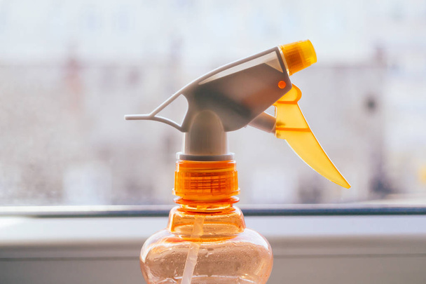 Close up spray bottle next to window. Household objects concept. - Фото, изображение