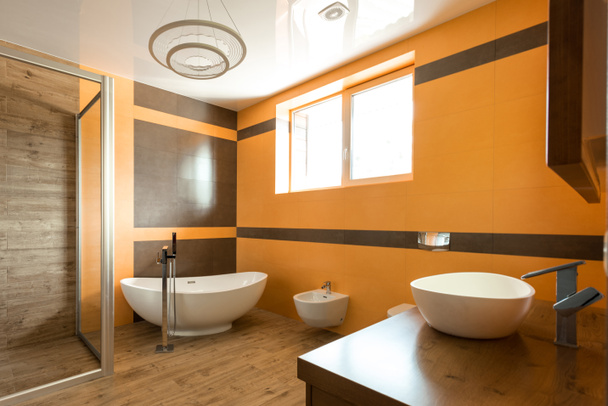 interior do banheiro em cores laranja e branco com banheira, pia e bidé
 - Foto, Imagem