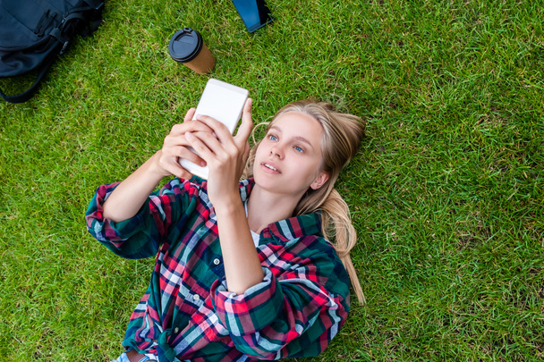 top view of young blonde woman lying on grass and using smartphone - Photo, Image