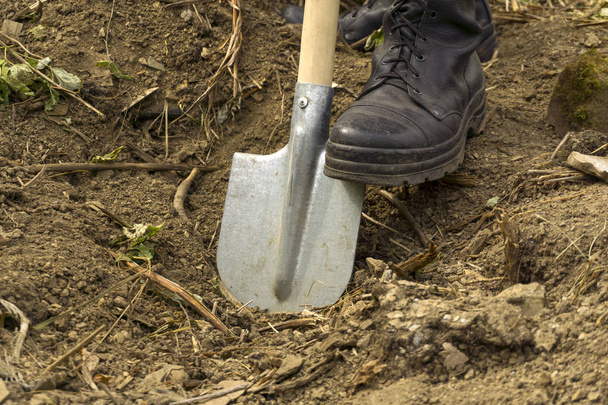 een man graaft een droge aarde met een spade - close-up van een voet in de kofferbak van een leger, rustend op een mes - Foto, afbeelding