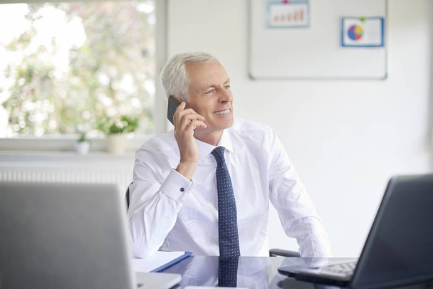 Executive senior businessman talking on smartphone while working laptop in office - Фото, зображення