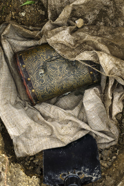 Vintage pecho desplegado de un paquete de tejido excavado desde el suelo, y herramienta de trinchera en el pozo
 - Foto, Imagen
