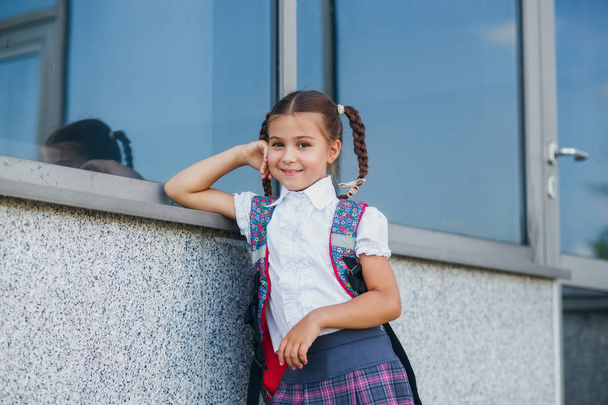 Pupil of primary school with book in hand. Girl with backpack near building outdoors. Beginning of lessons. First day of fall. - Foto, immagini